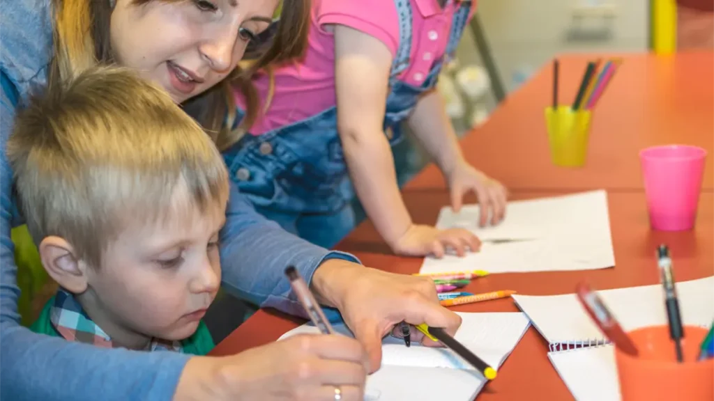 Bild på en ung kvinna som hjälper en liten pojke att rita.